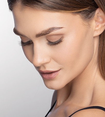 Model gleda dolje i smiješi se. Naglasak je na njezinim obrvama i trepavicama.